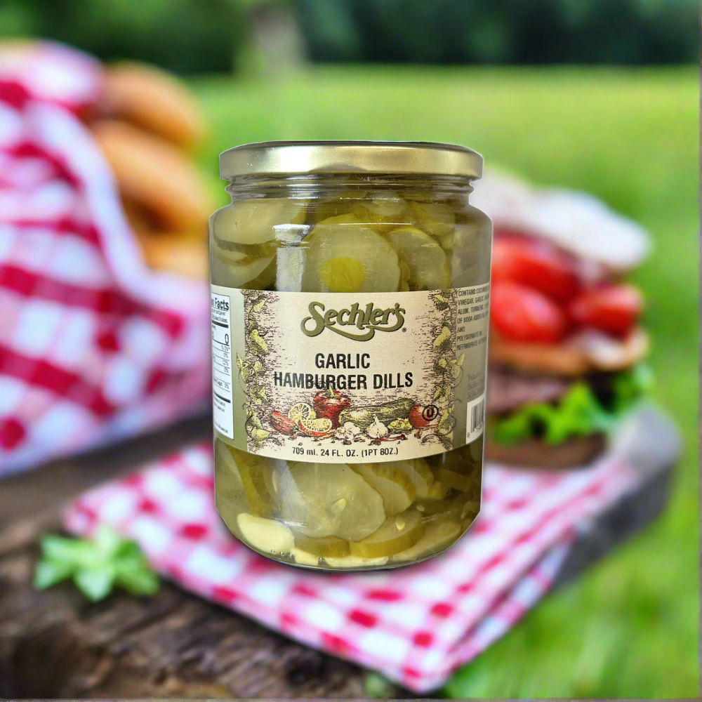 Jar of Garlic Hamburger Dills on picnic table with tablecloth and sandwiches.