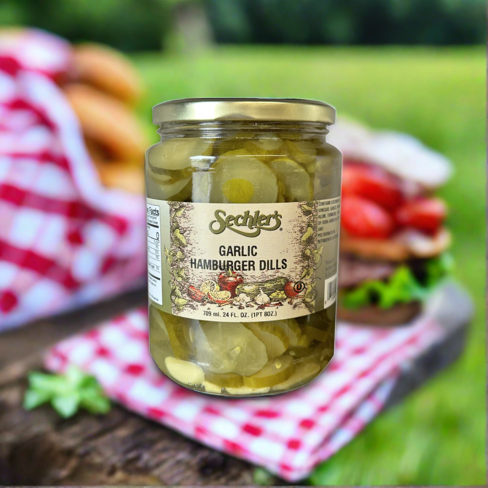 Jar of Garlic Hamburger Dills on picnic table with tablecloth and sandwiches. 