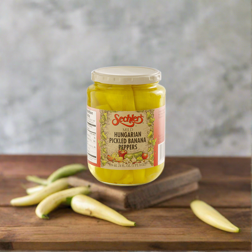 Jar of Mild Hungarian Banana Peppers on kitchen countertop surrounded by fresh banana peppers.